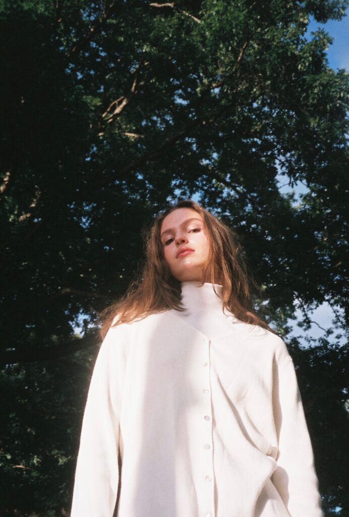 Photo of Sydney Brainard dressed in a white turtleneck set against the background of trees